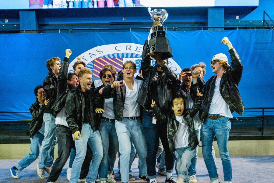 A group of collegiate men in leather jackets hoist a large trophy overhead in celebration